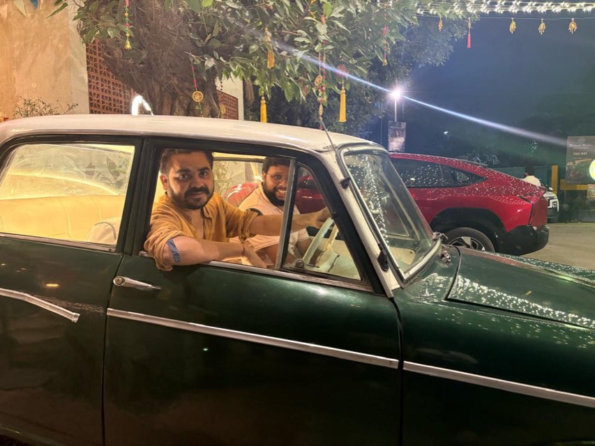 Two smiling customers in a vintage green classic car, enjoying self drive car rental in Greater Noida